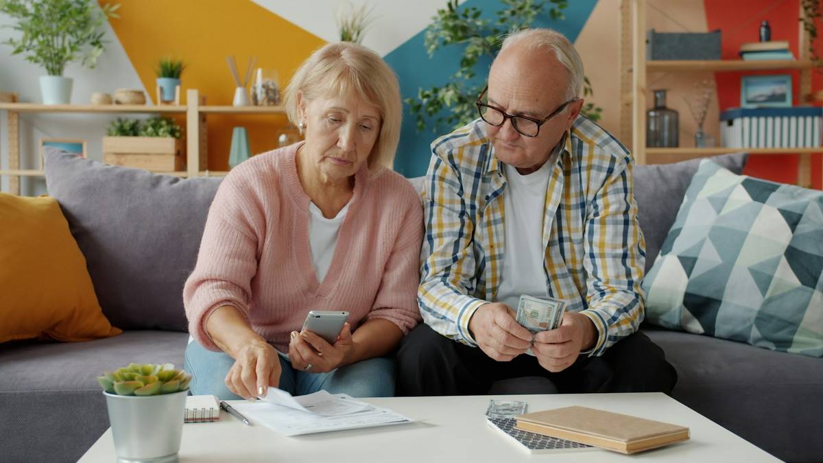 Older couple looking at bills and a phone while discussing finances